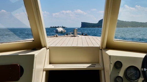 View from the cockpit of a motorboat cruising on Lake Garda with San Biagio Island and the Rocca di Manerba in the background