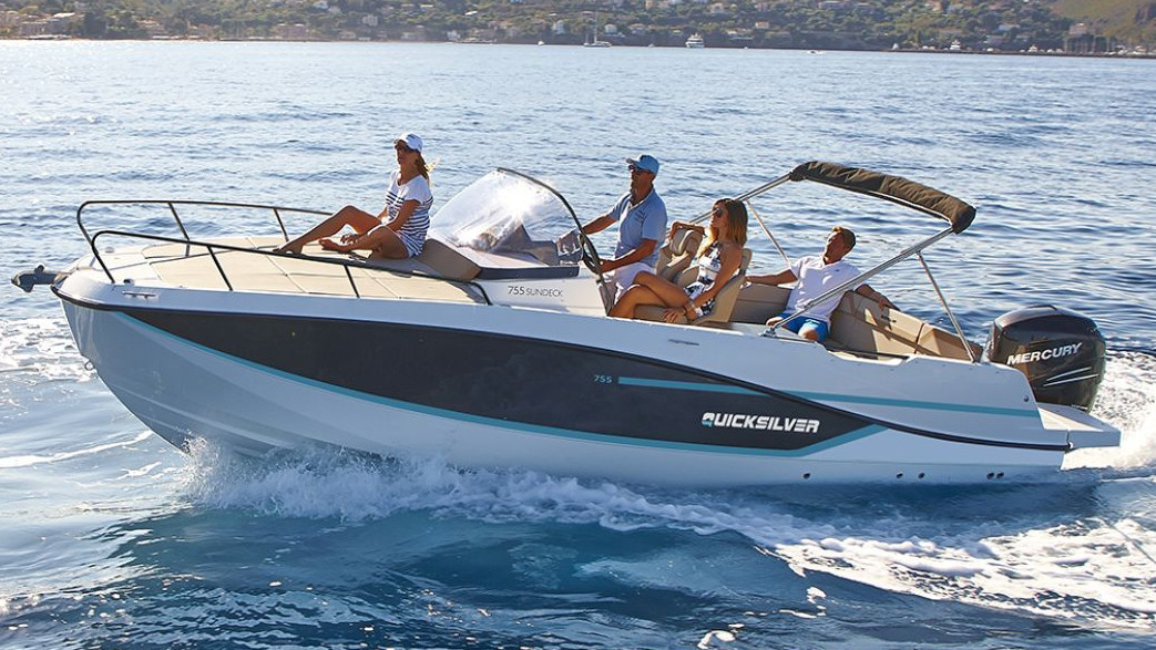Two couples of friends enjoying a sunny day on a rental boat, relaxing on the loungers, one person steering, and a woman lying on the front deck of the boat
