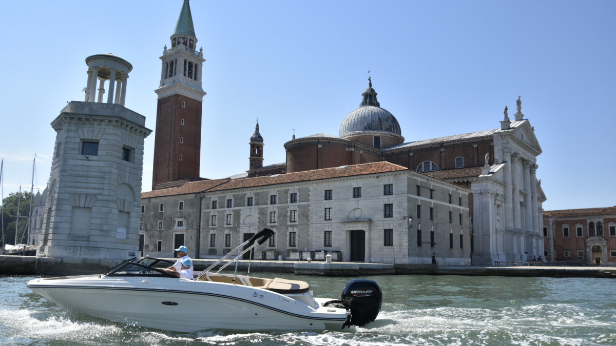 Man driving a rental motorboat in Venice waters with historic San Giorgio Maggiore church and Saint Mark'sbell tower in the background