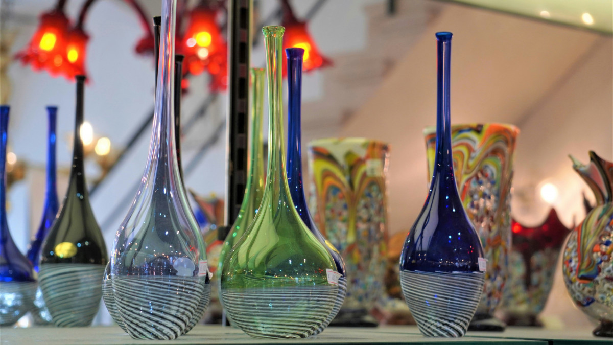 Hand-blown Murano glass vases with elegant long necks and striped patterns, displayed in a Venetian workshop