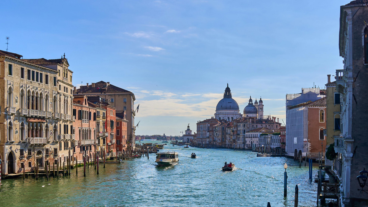 Panoramic view of the Grand Canal in Venice featuring historic palaces, gondolas, and the Santa Maria della Salute Basilica under a bright sky