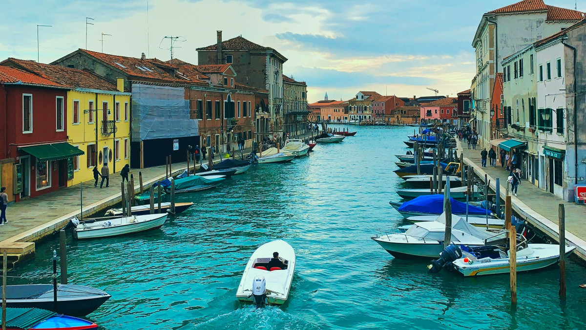 A motorboat cruising through a wide canal in Murano, Venice, lined with historic buildings and docked boats