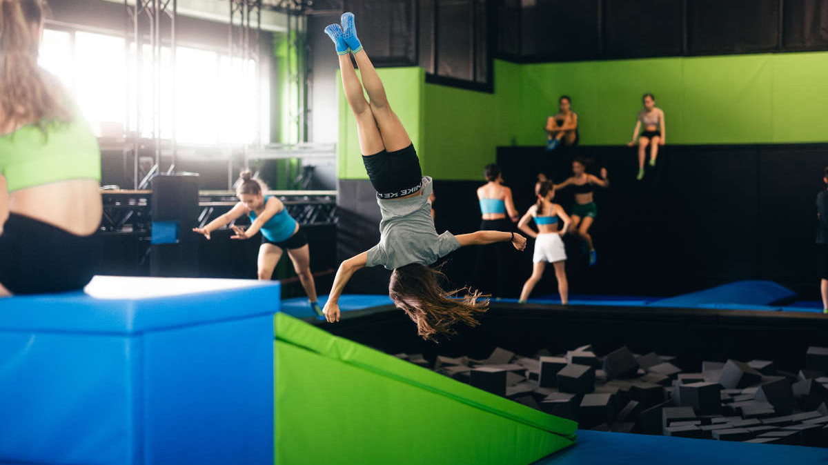 Professional indoor trampoline facility; person jumping and flipping into a safety foam cube pit.