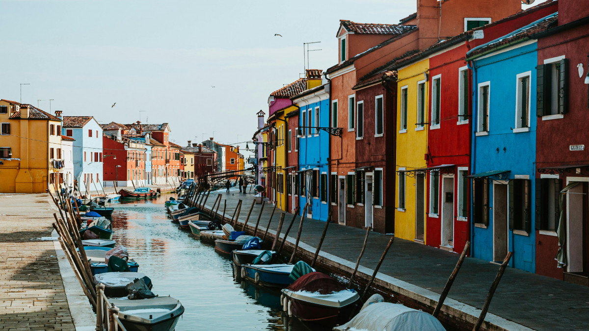 Burano island day trip from Jesolo; scenic view of the famous colorful houses of Venice and traditional blue fishing boats in the canal