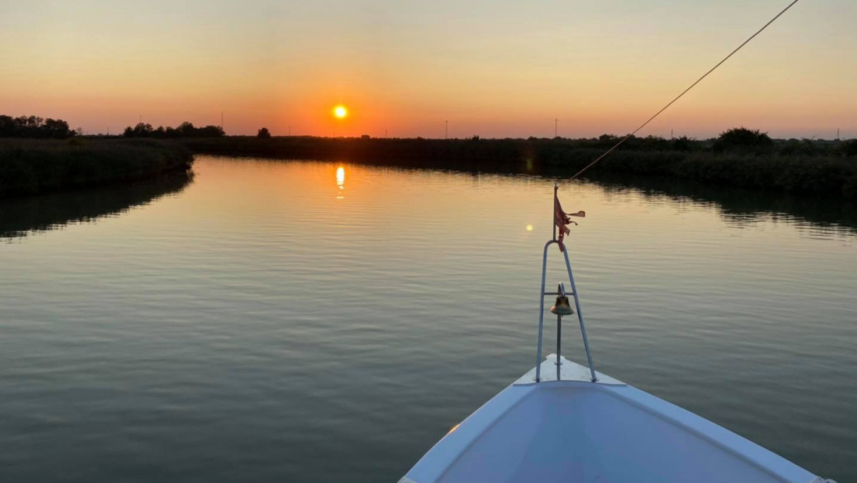 View from the bow of a boat sailing towards a golden sunset on the calm lagoon, with the sun reflecting on the water surface