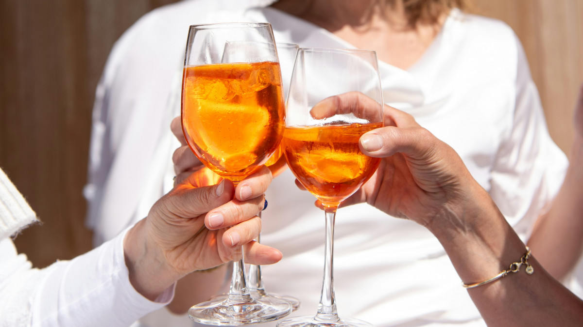 Close-up of three people toasting with bright orange Venetian Spritz cocktails during an aperitivo