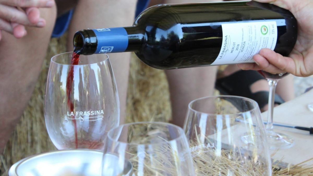 Red wine being poured from a "La Frassina" Merlot bottle into a glass during an outdoor tasting