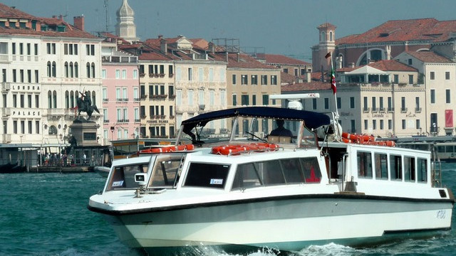 A white Marco Polo tour boat cruising on the turquoise water of the Grand Canal, with historic palaces and the Riva degli Schiavoni in the background
