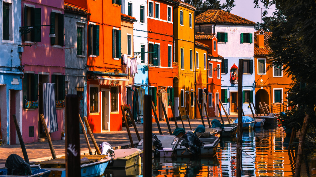 Rows of vibrant multi-colored houses along a canal with moored boats in Burano, Venice