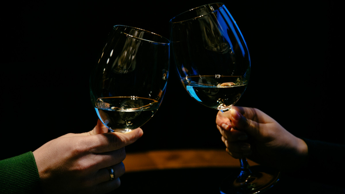 Two people clinking wine glasses with Prosecco wine against a dark background, celebrating a toast