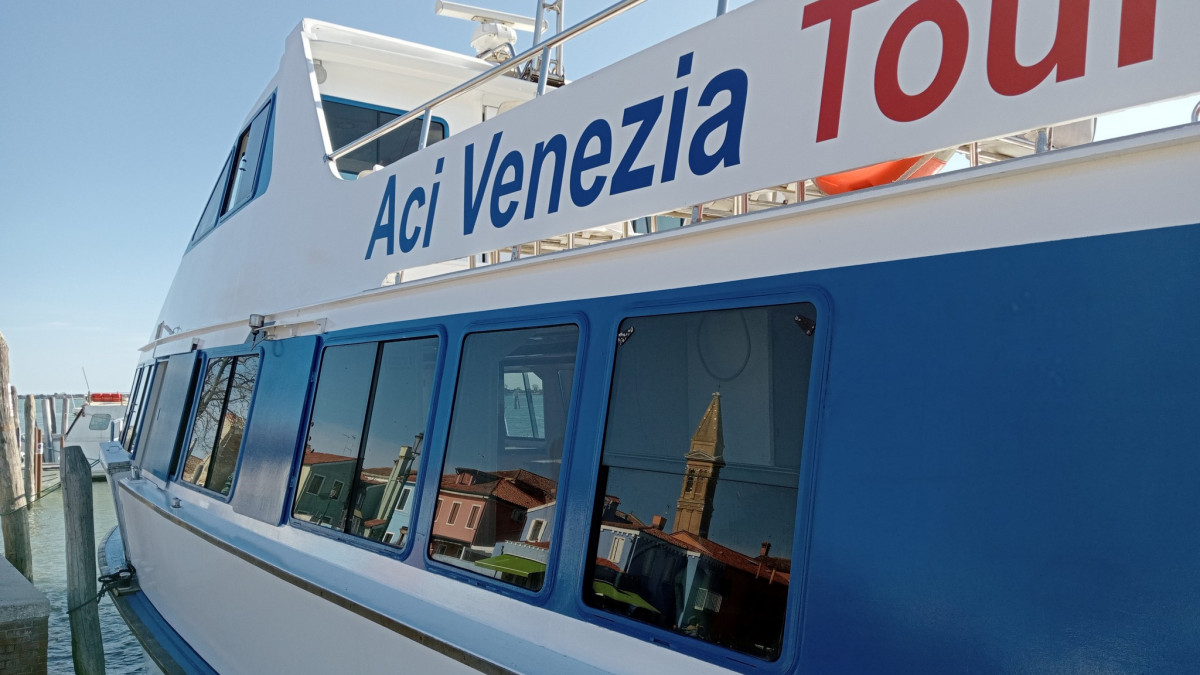 Close-up of an Aci Venezia Tourist boat with the reflection of a Venetian bell tower and colorful houses in its windows.