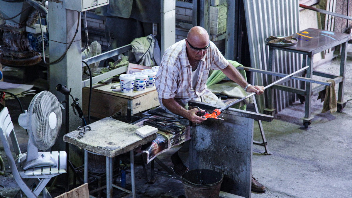 Experienced Murano glass master meticulously crafting a glass sculpture using traditional hand tools in a venetian furnace workshop.