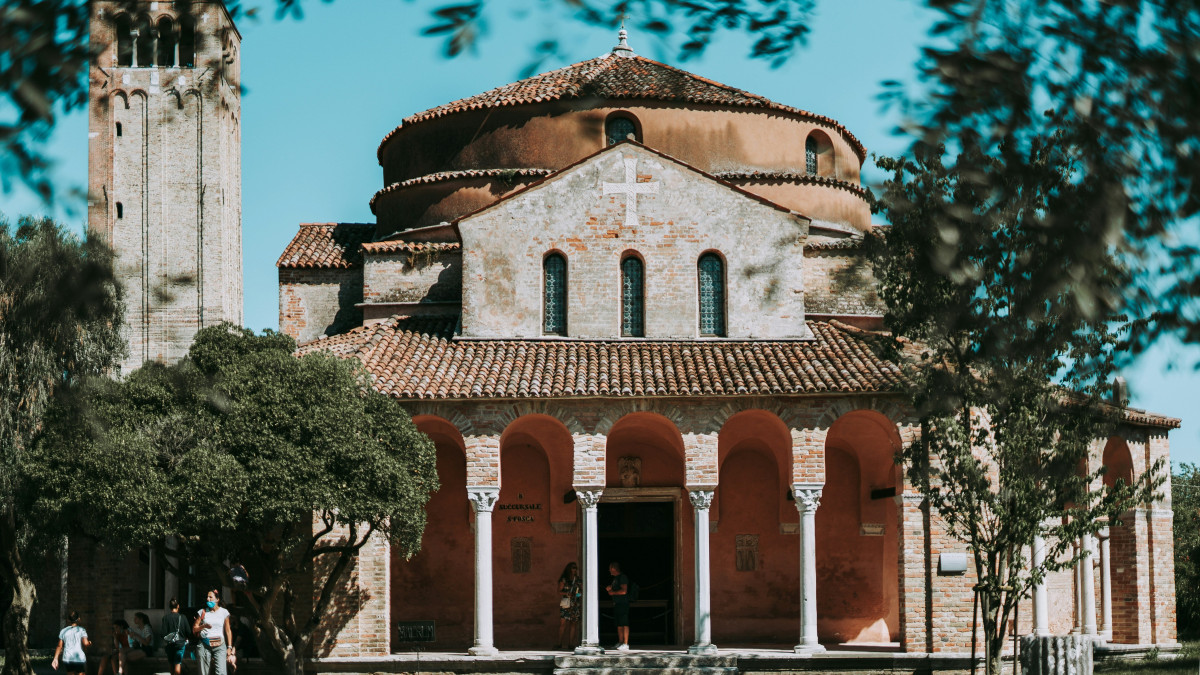 Exterior view of the Church of Santa Fosca in Torcello, Venice, featuring its unique circular Byzantine architecture and portico under a clear sky