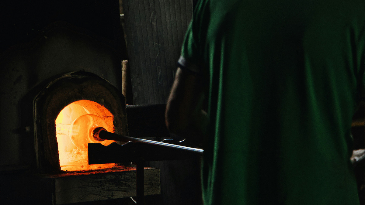Close-up of a glass artisan reheating a hand-blown glass piece in a glowing orange furnace inside a Murano workshop.