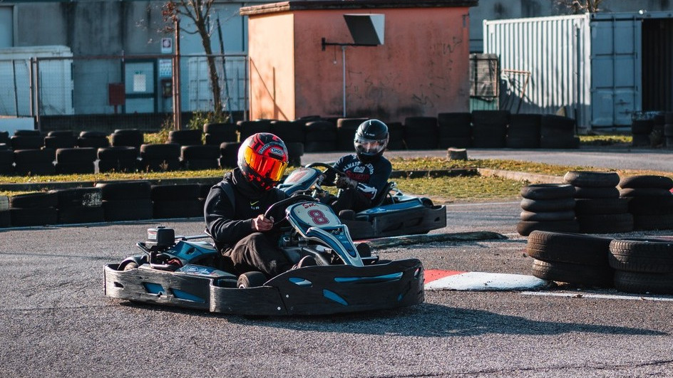 Two drivers in full safety gear racing blue Sodi go-karts around a corner at the Go-Kart Torracing outdoor circuit with tire barriers