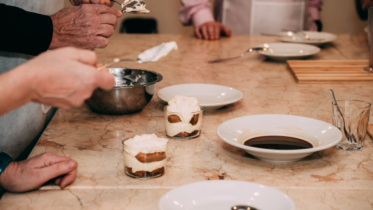 A participant assembling tiramisu, carefully layering creamy mascarpone and soaked savoiardi..