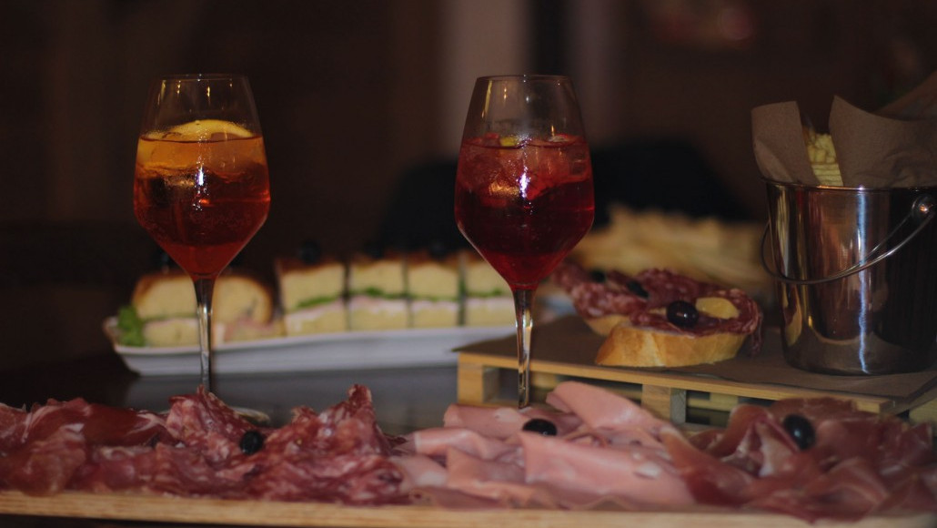 An authentic Italian aperitivo at Locanda Zanella featuring Spritz cocktails, fresh cold cuts, and traditional appetizers on a wooden platter.