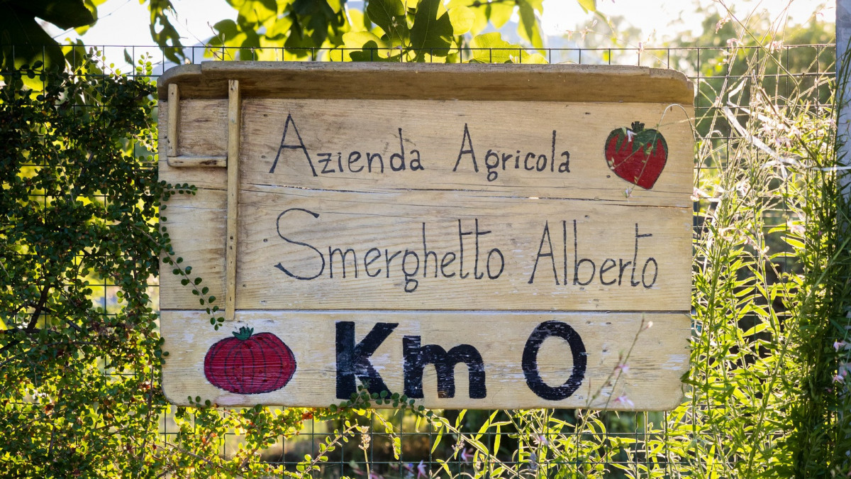 A rustic wooden sign for Azienda Agricola Smerghetto Alberto in Saccagnana, highlighting their "Km 0" local and sustainable farming philosophy.