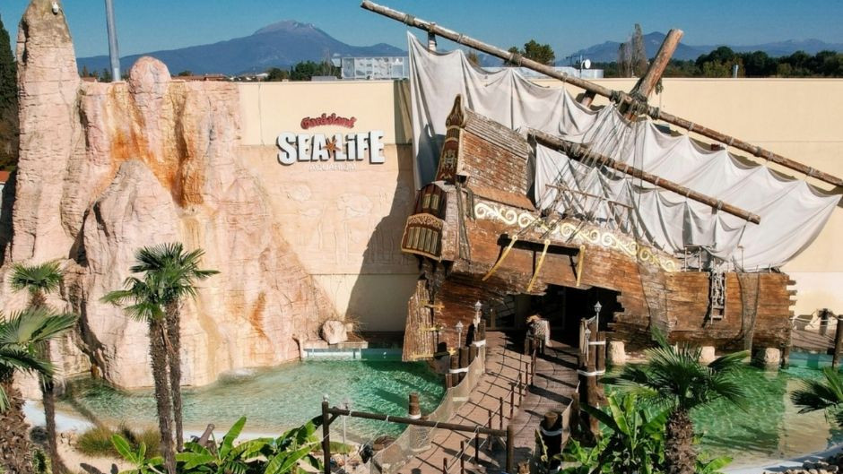The themed entrance of Gardaland SEA LIFE Aquarium featuring a large wooden pirate shipwreck and artificial rock formations.