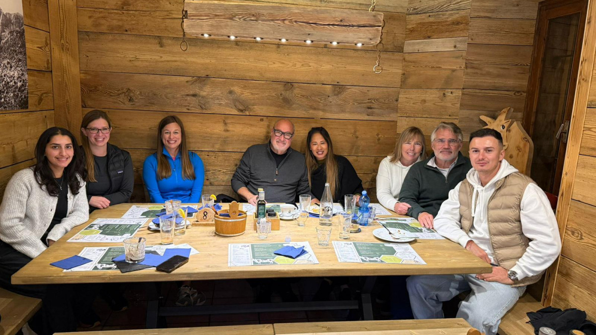 A diverse group of people enjoying a traditional meal inside a rustic wood-paneled mountain hut restaurant in the Italian Dolomites.