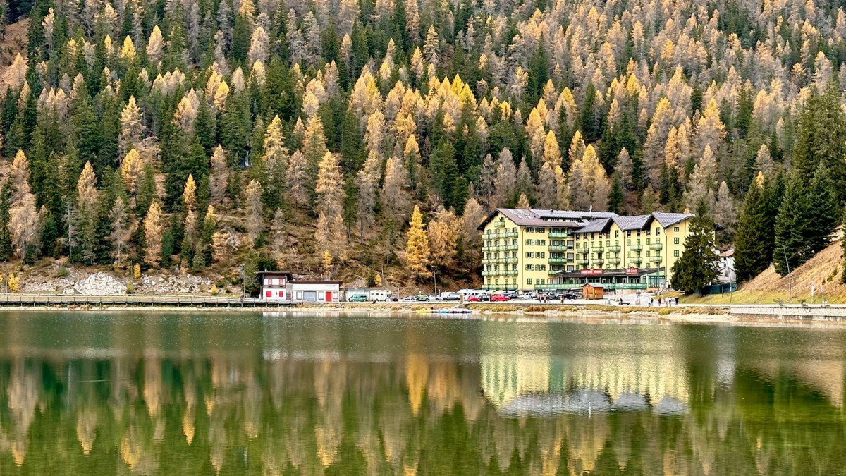 Golden autumn trees and the Grand Hotel Misurina reflected in the calm waters of Lake Misurina in the Italian Dolomites.