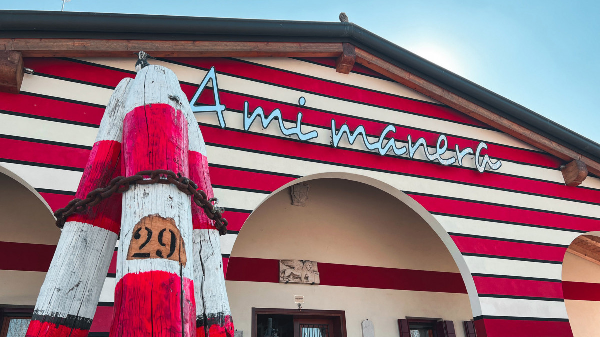 Exterior of Cantina A Mi Manera winery in Portogruaro, featuring red and white striped walls and a traditional Venetian canal mooring post (briccola).