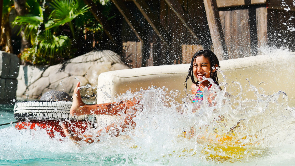 A young girl laughing and splashing in the water at Caneva Acquapark, enjoying a fun water slide experience during a summer day..