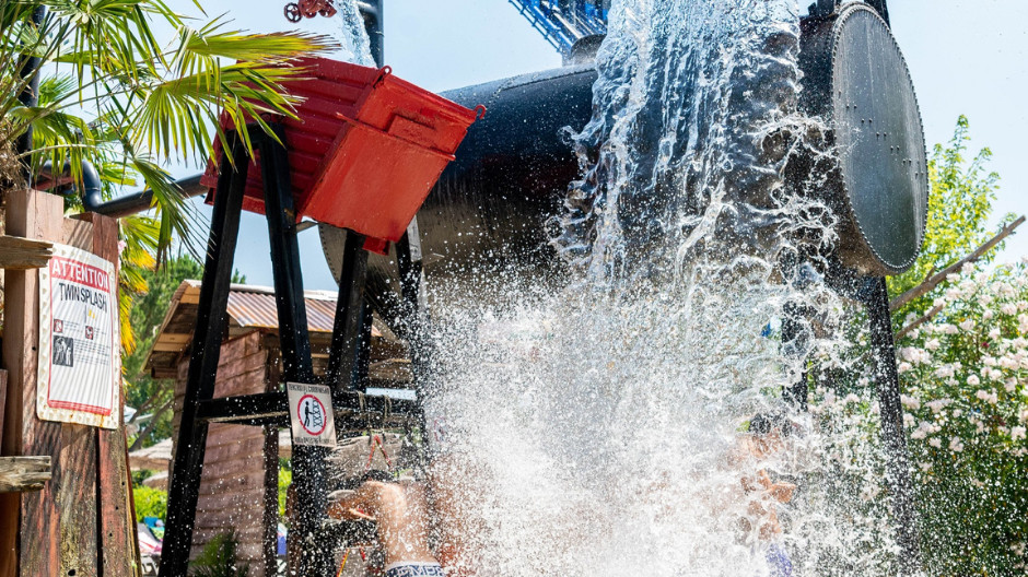 Massive water splash at the Twin Splash attraction in Caneva Acquapark, featuring giant tipping buckets and industrial-themed water play for families.