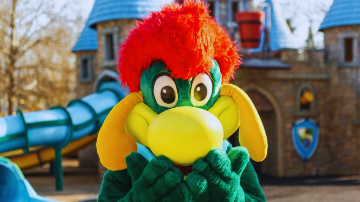 Prezzemolo mascot posing in front of a medieval stone castle with a blue slide at Gardaland Park, Italy.