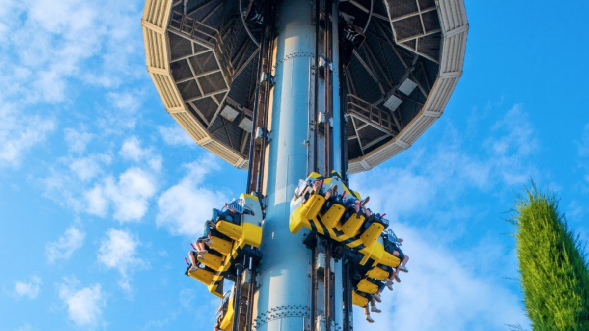 Riders experiencing the thrill of Space Vertigo drop tower at Gardaland Park, Italy, against a blue sky with scattered clouds.