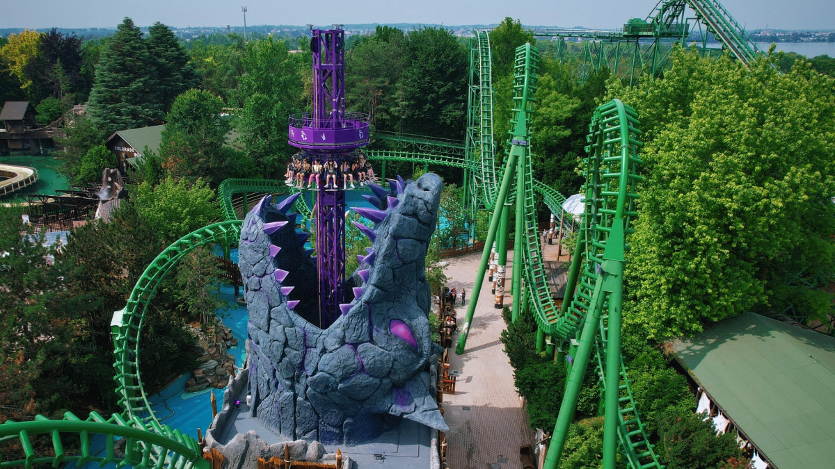 High-angle view of Wolf Legend drop tower and Shaman double-loop roller coaster with green tracks at Gardaland Park, Italy.
