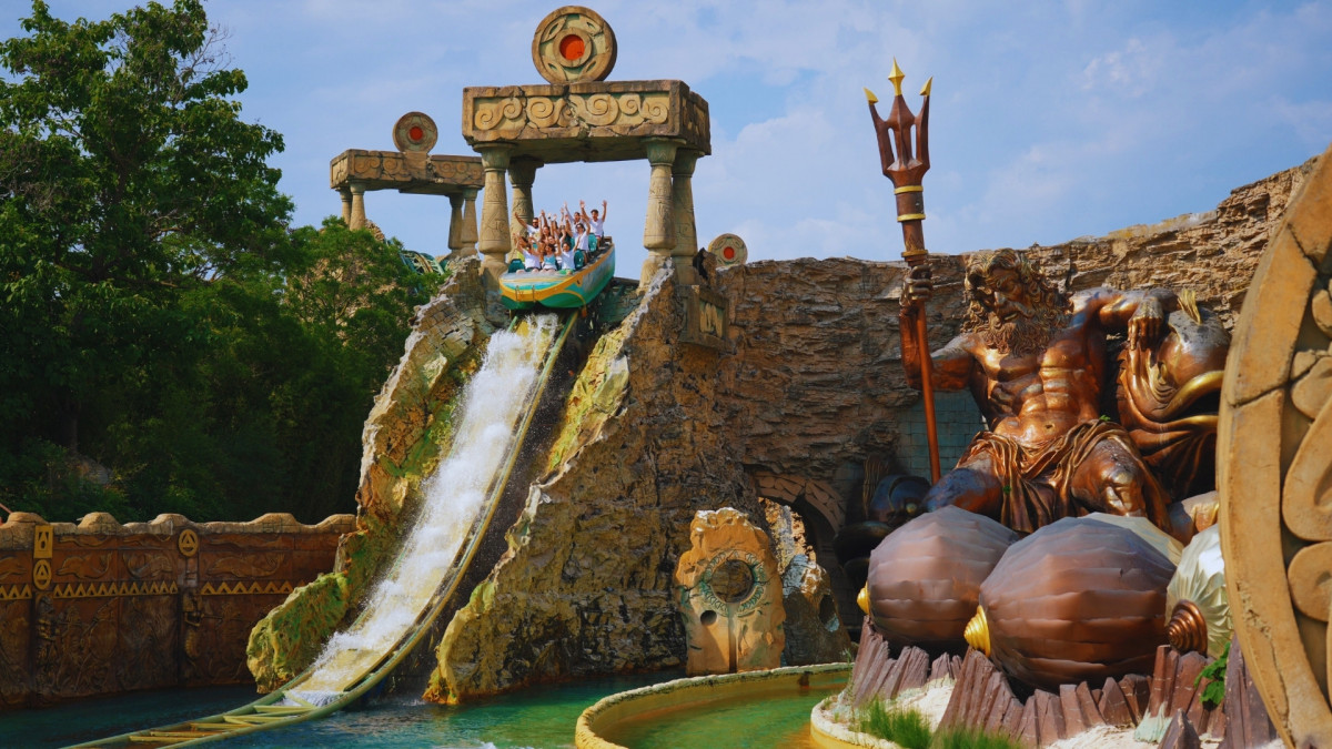 The Fuga da Atlantide water ride at Gardaland Park in Italy, featuring a large splash from a boat drop between giant Neptune statues and ancient ruins.