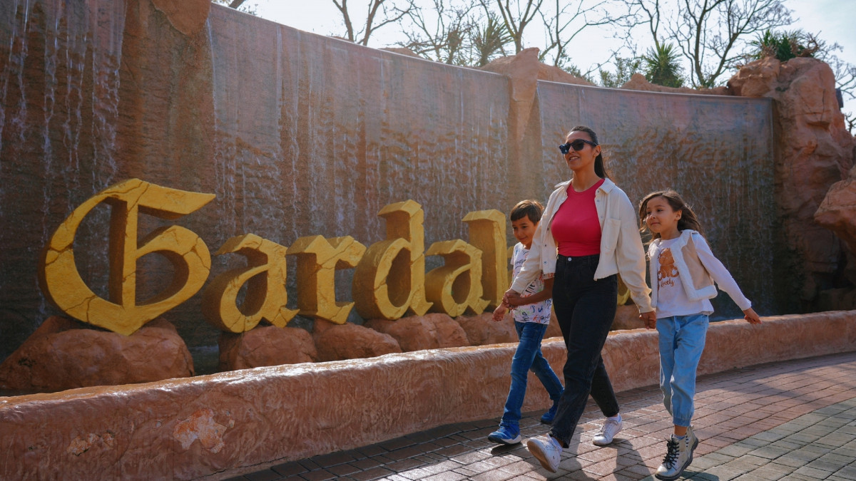A mother and two children walking past the iconic golden Gardaland sign with a waterfall background at Gardaland Resort in Italy.