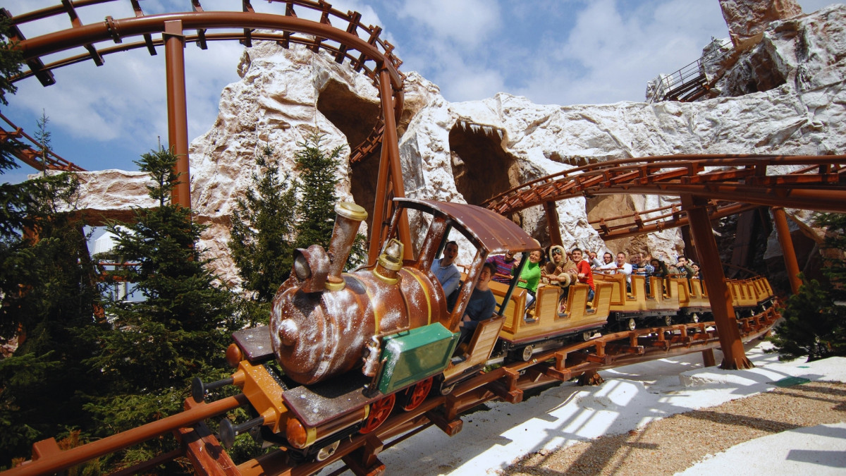 The Mammut family roller coaster at Gardaland Park, Italy, featuring a steam train-themed car traveling through a snowy Arctic landscape with rocky mountains.