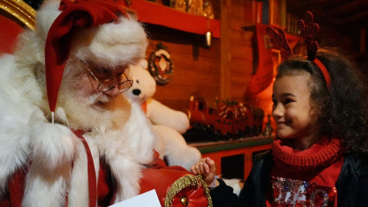 A young girl smiling while interacting with Santa Claus in his magical Christmas grotto during Gardaland Magic Winter, Italy.