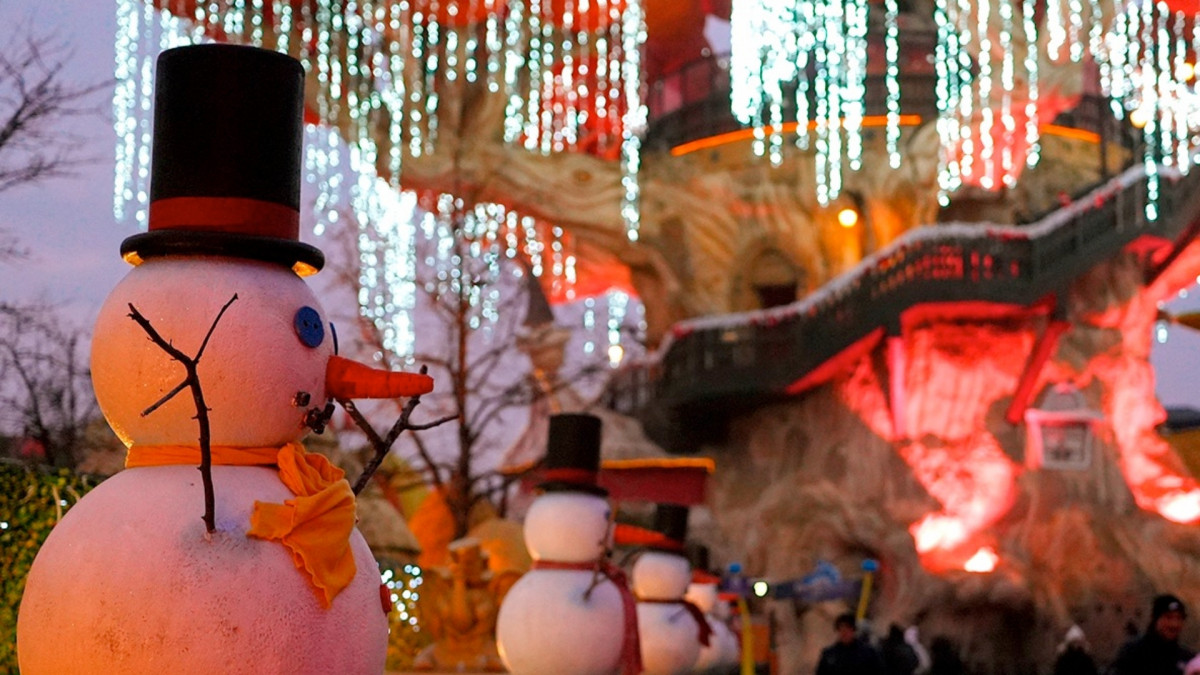 Row of decorative snowmen with top hats and orange scarves leading to the illuminated Magic Tree during Gardaland Magic Winter at sunset.