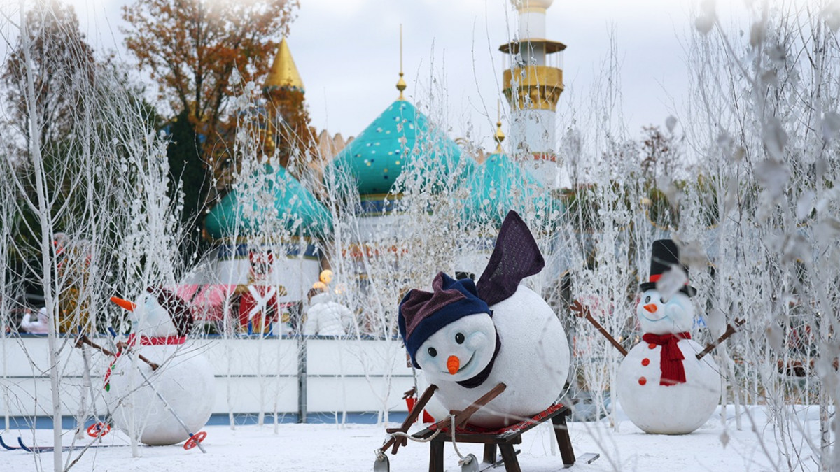 Decorative snowmen figures on a sled and skiing in a snowy landscape with white trees and colorful park buildings at Gardaland Magic Winter.