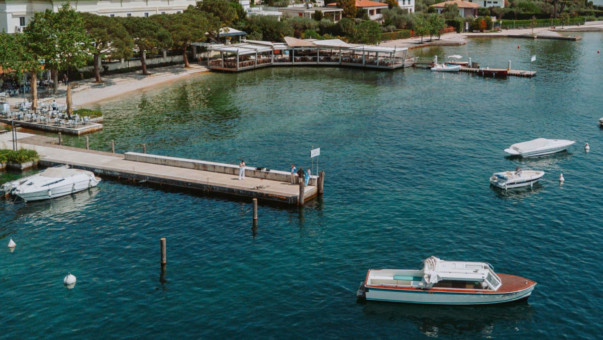 Bertoldi Boats motorboat tour at a scenic pier in San Felice del Benaco, Lake Garda, with lakeside restaurants in the background.