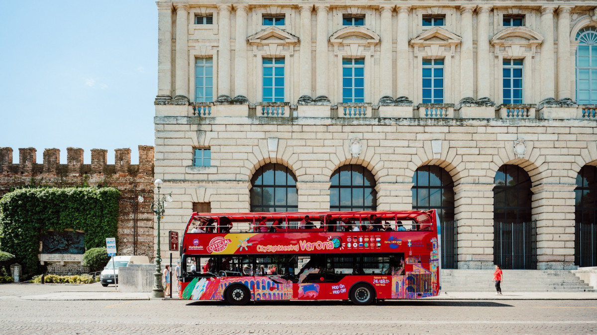 Red City Sightseeing Verona hop-on hop-off bus parked in front of the historic Palazzo della Gran Guardia in Verona, Italy