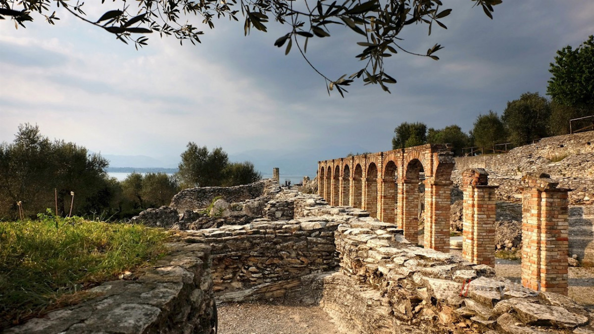 Ancient Roman stone ruins and brick arches at Grotte di Catullo in Sirmione, with a scenic view of Lake Garda.
