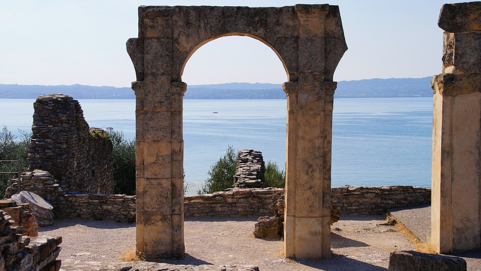Ancient stone arch at the Grotte di Catullo Roman villa ruins, framed view of Lake Garda in Sirmione, Italy.