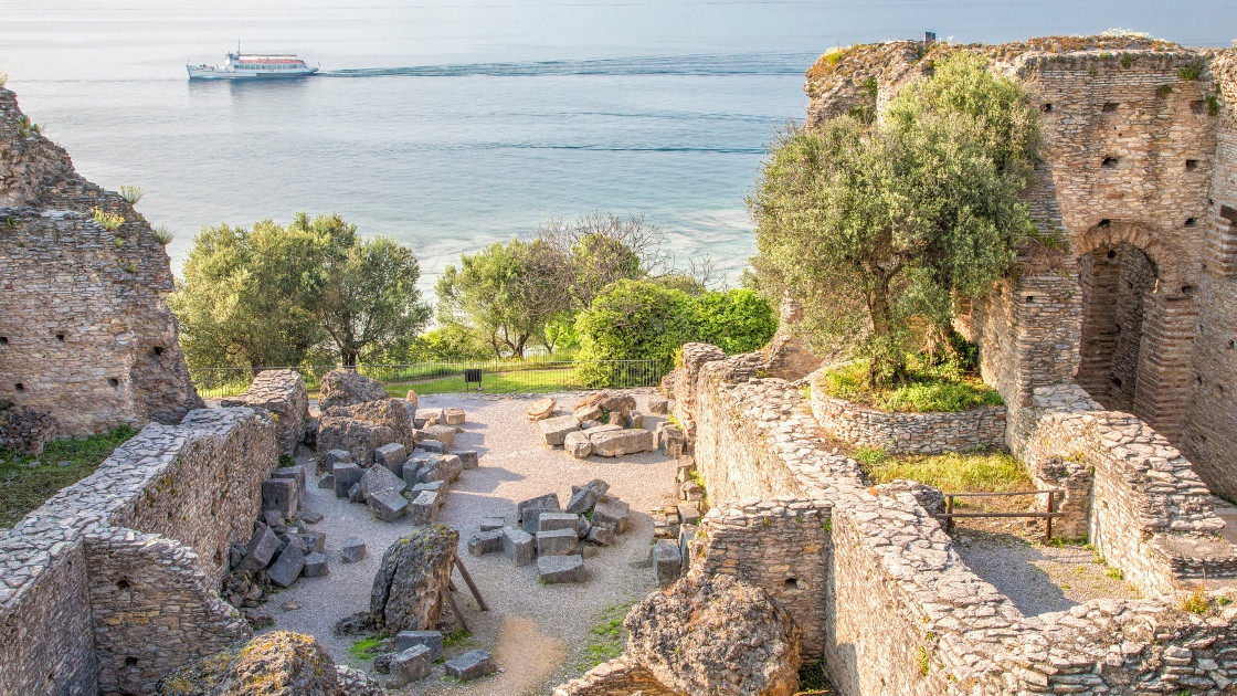 Ancient Roman Grotte di Catullo ruins overlooking Lake Garda in Sirmione, Italy, with a boat sailing in the background