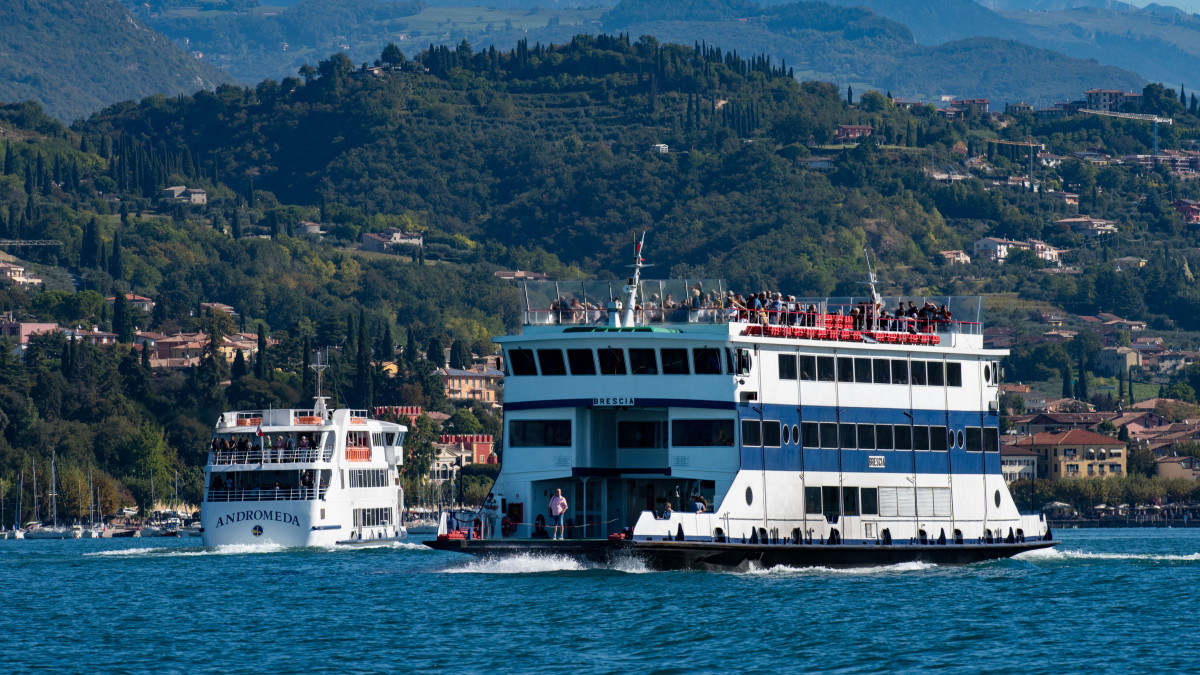 The Andromeda and Brescia ferries of Navigarda fleet cruising on Lake Garda with coastal hills in the background.