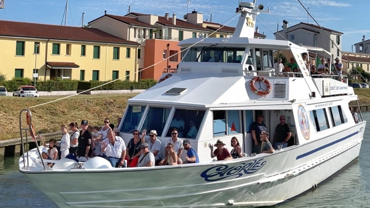 Tourist sightseeing boat with passengers cruising through a canal in Caorle, Italy.