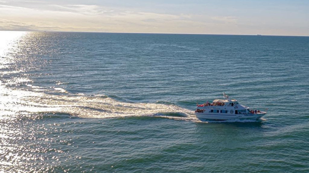 A Caorle excursion boat cruising the Adriatic Sea, with a white wake and sun reflection, Italy.