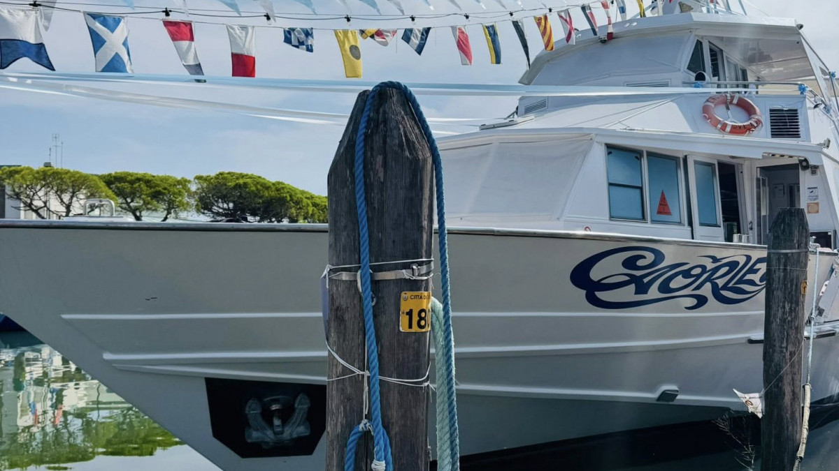 Close-up of a white motor yacht named "Caorle" moored at a marina in Caorle, Italy, featuring a line of colorful nautical signal flags.
