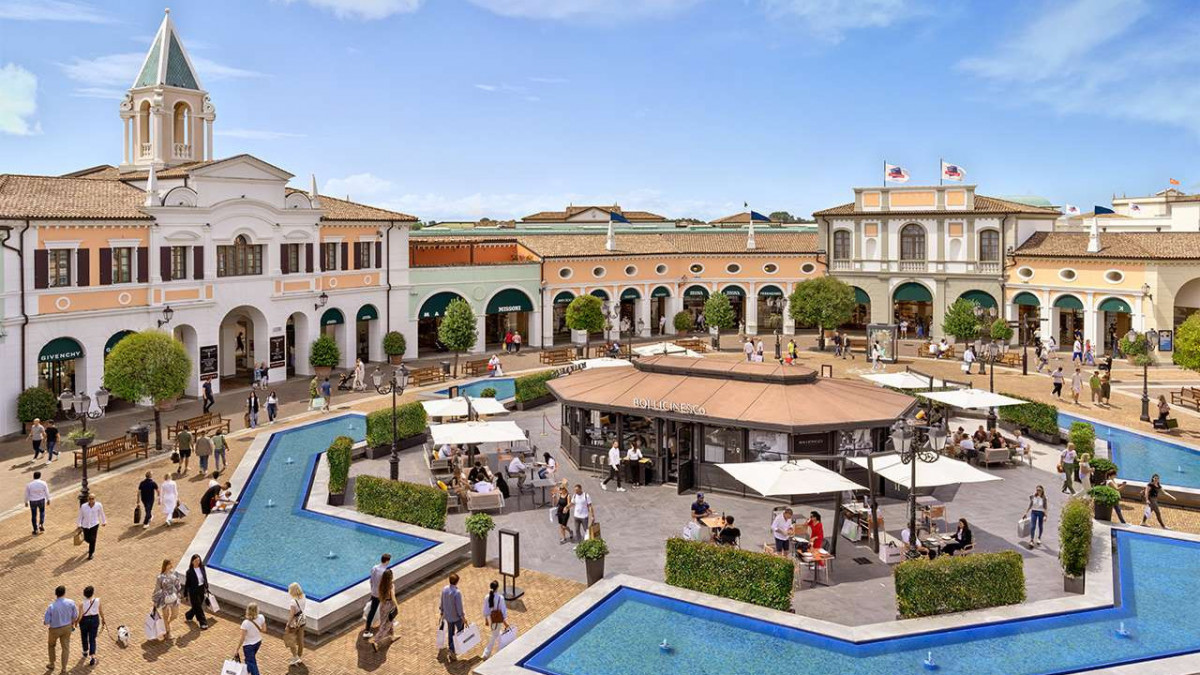 Panoramic view of the central square at Noventa di Piave Designer Outlet featuring fountains, outdoor cafes, and luxury brand stores.