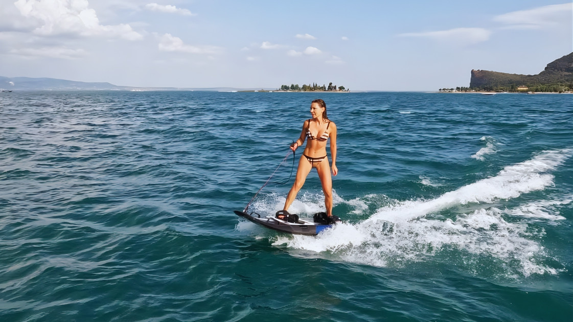 Woman riding a motorized Jetboard on Lake Garda with Isola del Garda and Rocca di Manerba in the background.