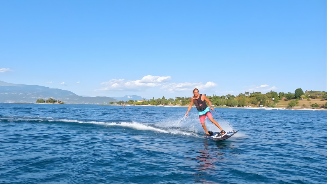 Man riding a motorized surfboard at full speed on Lake Garda with San Biagio Island (Rabbit Island) in the background.