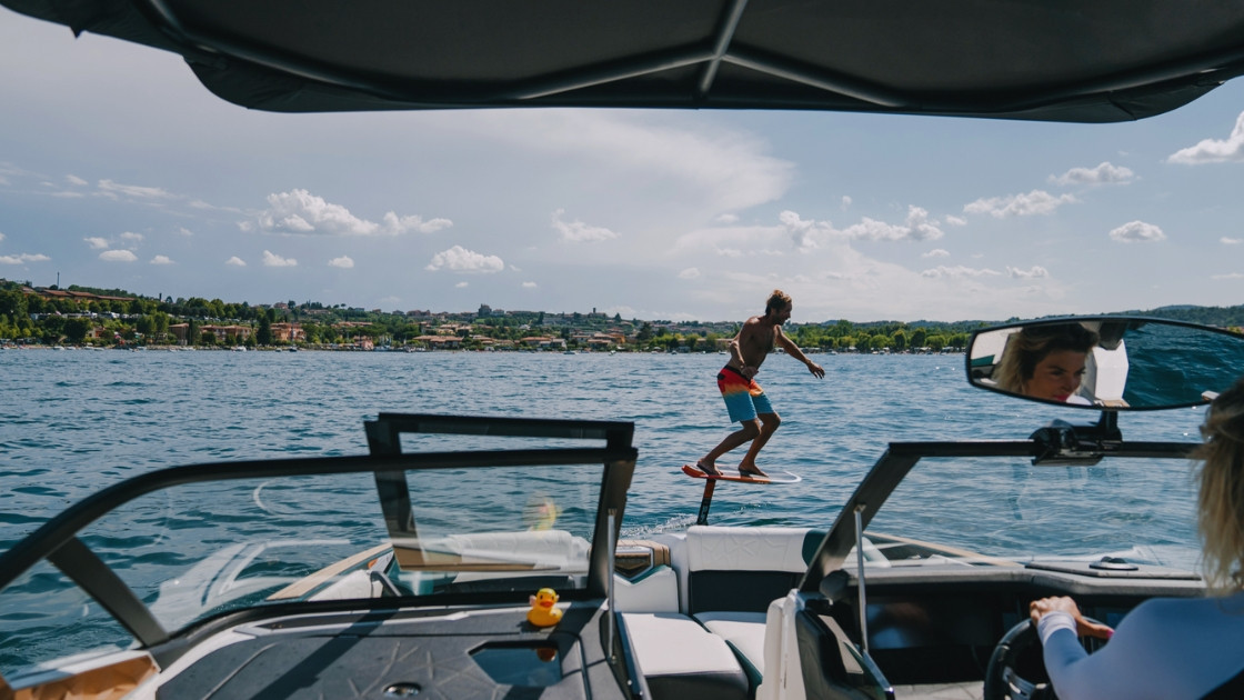 Perspective view from a support boat of a man hydrofoil surfing on Lake Garda